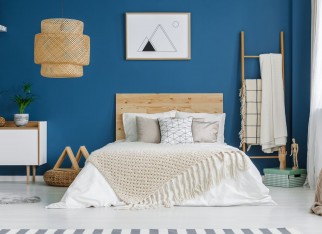 Knit blanket on wooden bed in blue bedroom interior with poster on the wall and lamp