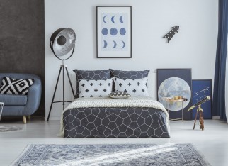 Patterned pillow on blue couch in spacious bedroom interior with telescope and lamp near bed