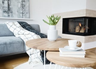 Patterned blanket on grey sofa and flowers on a table in warm living room interior with fireplace
