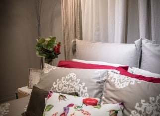 Bedroom interior in soft light with colorful pillows. Modern lamp and vase of fake flowers on the bedside table.