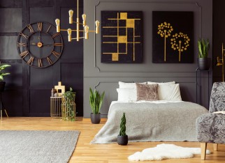 Real photo of golden accents, clock, paintings, plants and double bed in a dark bedroom interior