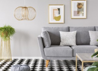 Real photo of a living room interior with gold posters on the walls, grey sofa with cushions and checkered floor