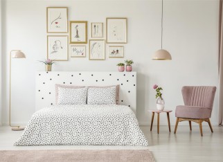 Pastel lamp above table with flower and pink armchair in woman's bedroom interior with bed