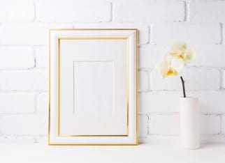 Gold decorated frame mockup with soft yellow orchid in vase. Empty frame mock up for presentation artwork. Template framing for modern art.