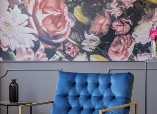 Royal blue armchair with gold frame standing on carpet in real photo of grey sitting room interior with gold lamp and floral wallpaper