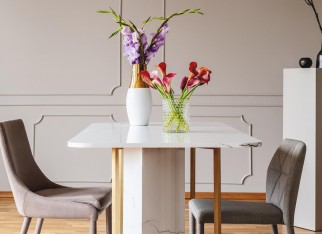 Flowers on table in grey dining room interior with gold lamp and chairs on carpet. Real photo