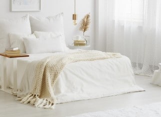 White bedroom interior with windows, gold accessories and white bedsheets on king-size bed