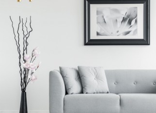 Plant next to grey couch in living room interior with checkered floor and poster. Real photo